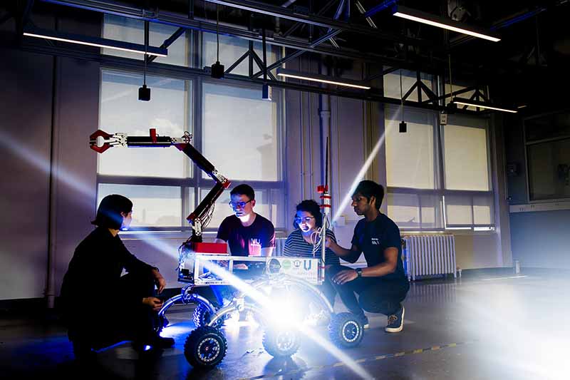 four students work on rover robot in warehouse